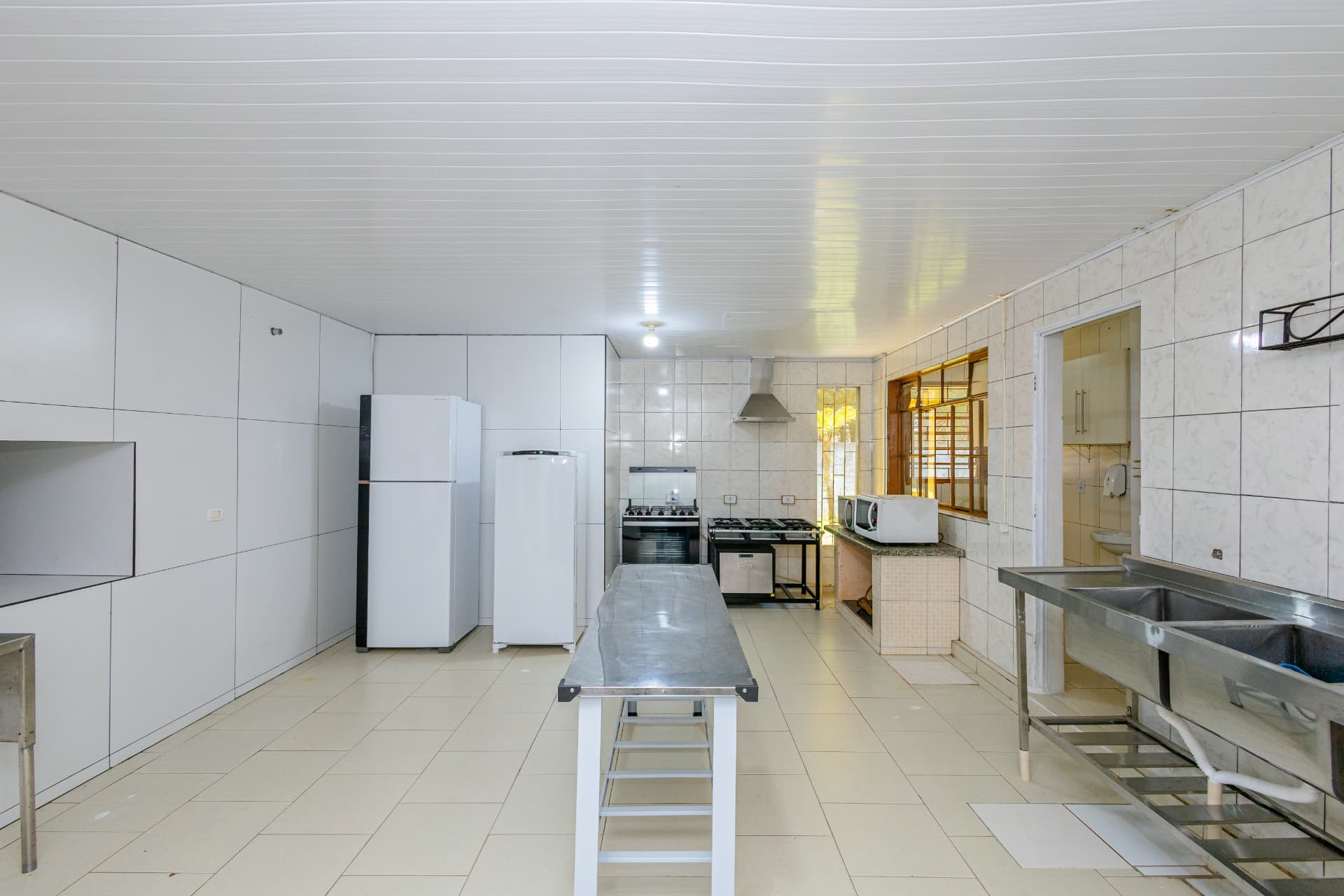 Cozinha com bancada central de aço inox, fogões e geladeiras